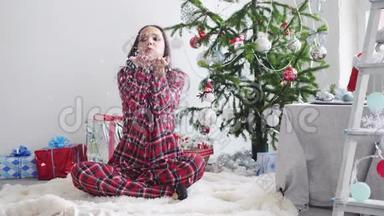 快乐的女孩吹着杉木圣诞树和工作室的窗户的纸屑。 慢动作。 3840x2160。 圣诞节概念